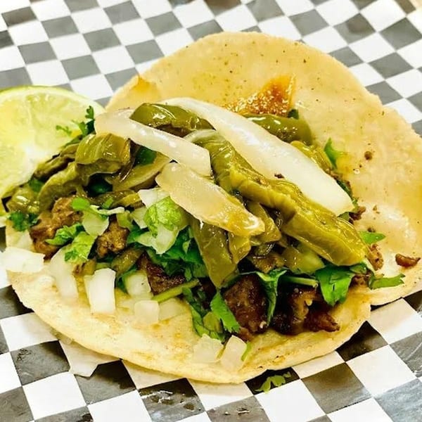 A single taco with meat, green peppers, onions, and cilantro, served with a lime wedge.
