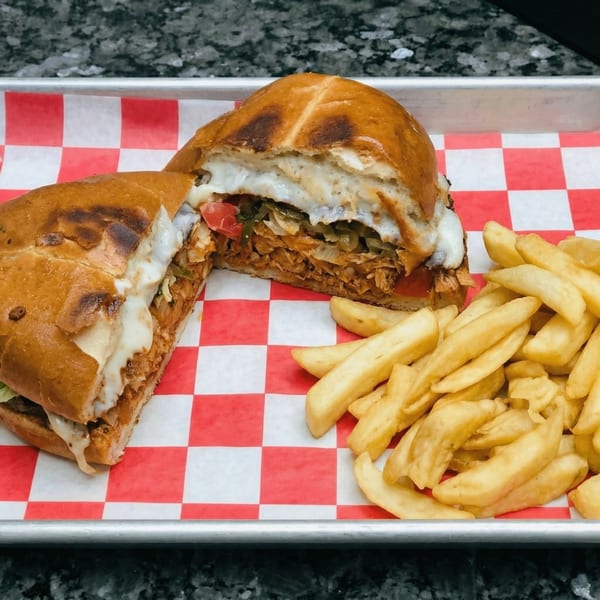 A sliced torta sandwich with melted cheese and filling, served with a side of french fries.