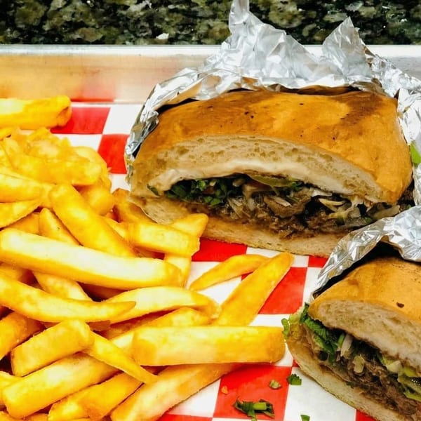 Two foil-wrapped sandwiches with meat and greens, served with golden french fries on a red and white checkered paper.