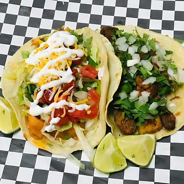 Two tacos with various toppings and lime wedges on a black and white checkered surface.