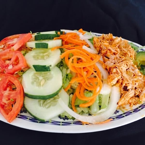 A vibrant salad with shredded chicken, sliced tomatoes, cucumbers, carrots, and onions on a white plate.