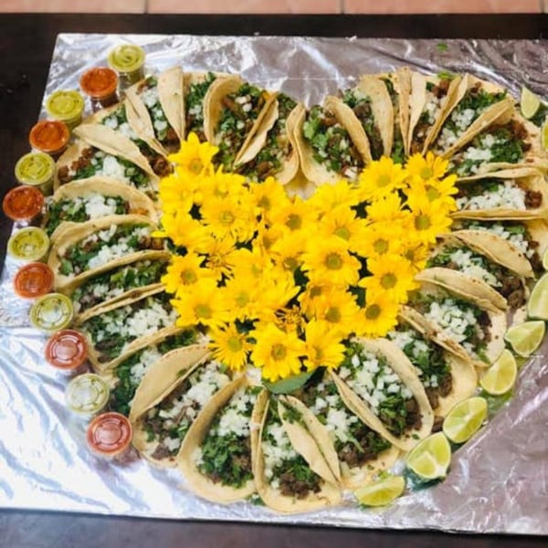 Heart-shaped arrangement of tacos with cilantro, onions, lime wedges, and small sauce cups.