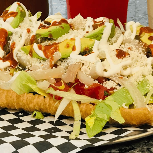 A large, loaded Mexican dish with lettuce, tomatoes, avocado, cheese, and sauces on a checkered paper.