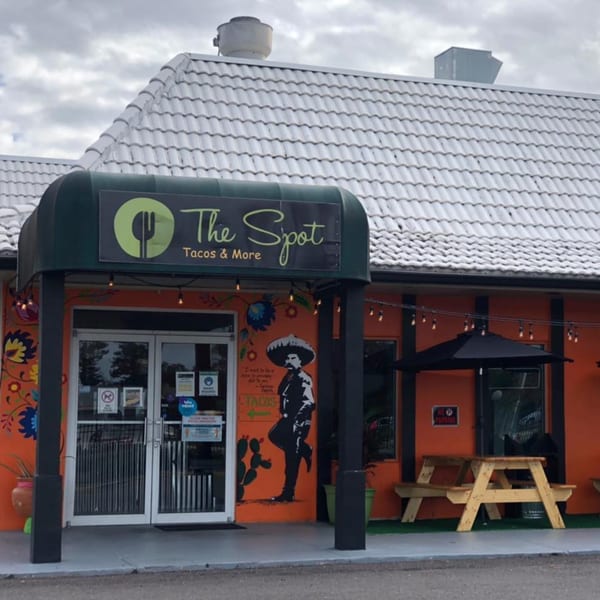 The Spot Tacos & More restaurant exterior with orange walls, a green awning, and outdoor seating.
