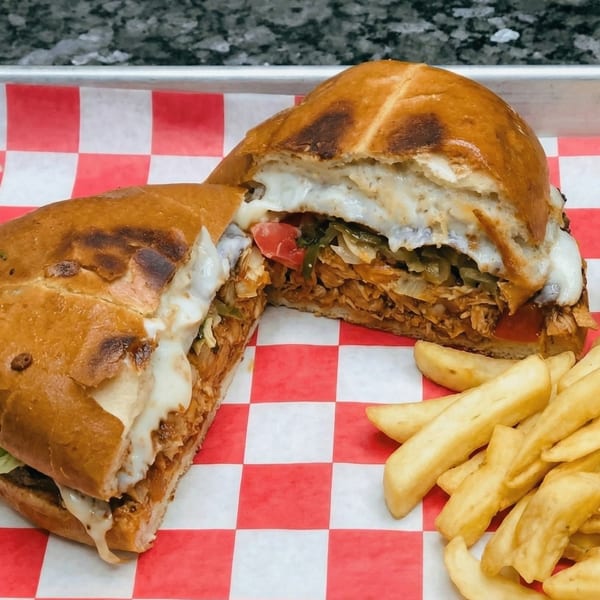 A large sandwich, cut in half, with melted cheese, meat, and vegetables, served with fries.