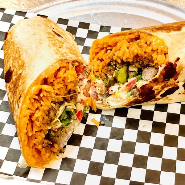 A large burrito, cut in half, revealing rice, meat, and vegetables on checkered paper.